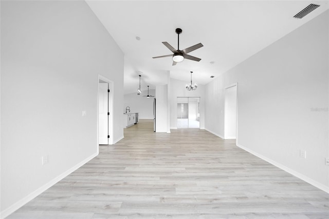 unfurnished living room with ceiling fan with notable chandelier, high vaulted ceiling, and light hardwood / wood-style flooring