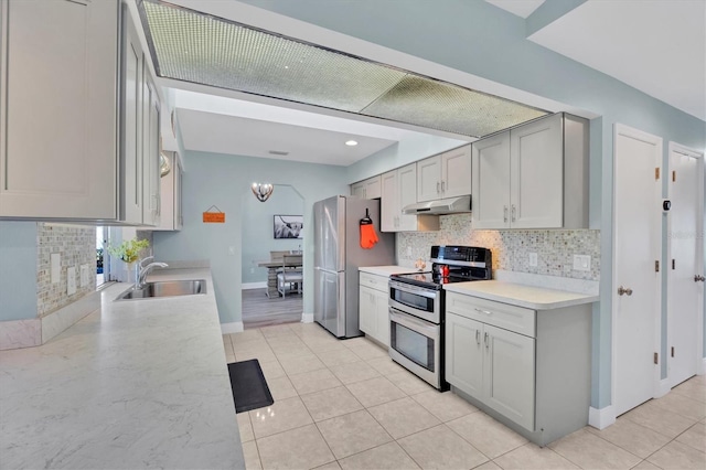 kitchen with stainless steel appliances, light countertops, light tile patterned flooring, a sink, and under cabinet range hood