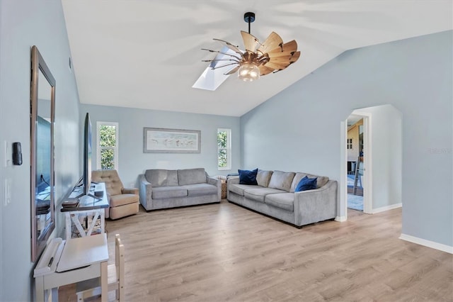 living room featuring light wood-type flooring, vaulted ceiling with skylight, baseboards, and ceiling fan