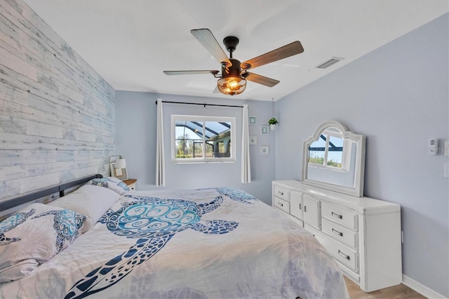 bedroom with wooden walls, an accent wall, a ceiling fan, baseboards, and visible vents