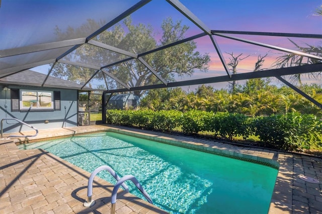 pool at dusk featuring glass enclosure, an outdoor pool, and a patio