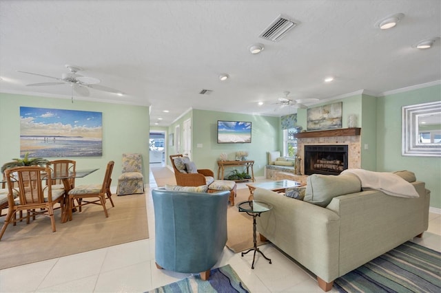 living room with ceiling fan, light tile patterned flooring, crown molding, and a tiled fireplace