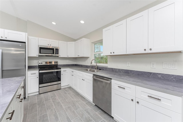 kitchen with stainless steel appliances, white cabinetry, sink, and vaulted ceiling