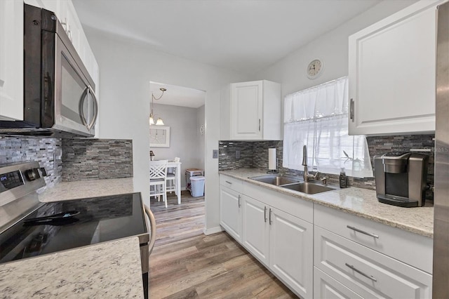 kitchen featuring decorative backsplash, appliances with stainless steel finishes, sink, white cabinetry, and hanging light fixtures