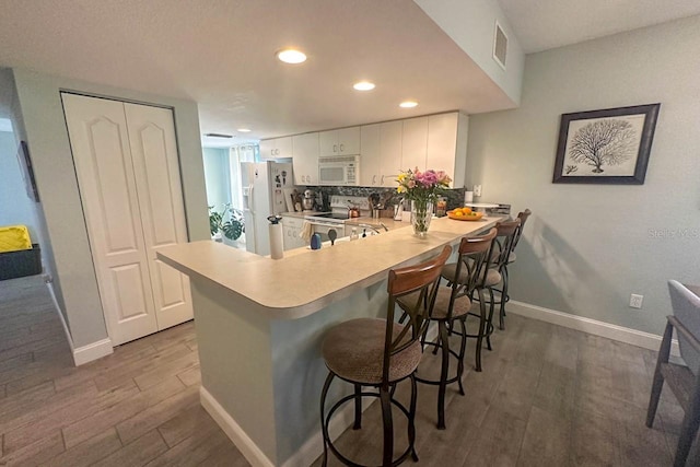 kitchen featuring white cabinetry, dark wood-type flooring, a kitchen breakfast bar, kitchen peninsula, and white appliances