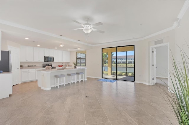 kitchen with appliances with stainless steel finishes, ornamental molding, a kitchen island with sink, ceiling fan, and white cabinets