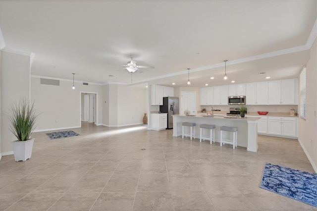 interior space featuring stainless steel appliances, ceiling fan, crown molding, white cabinetry, and an island with sink