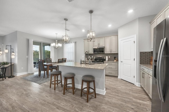 kitchen with light stone countertops, decorative light fixtures, stainless steel appliances, sink, and a center island with sink