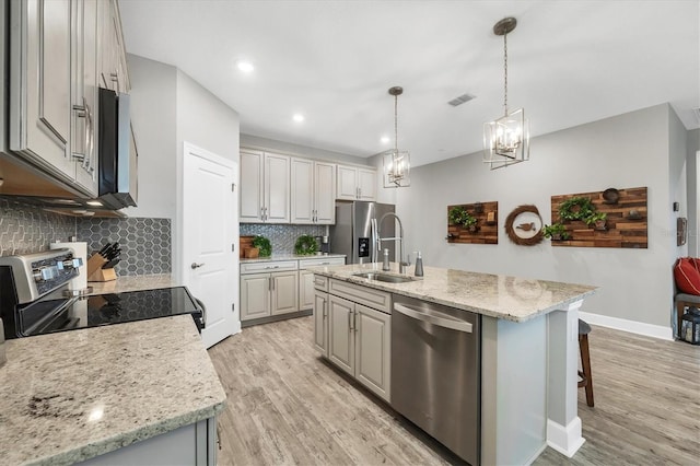 kitchen featuring pendant lighting, appliances with stainless steel finishes, decorative backsplash, sink, and a kitchen island with sink