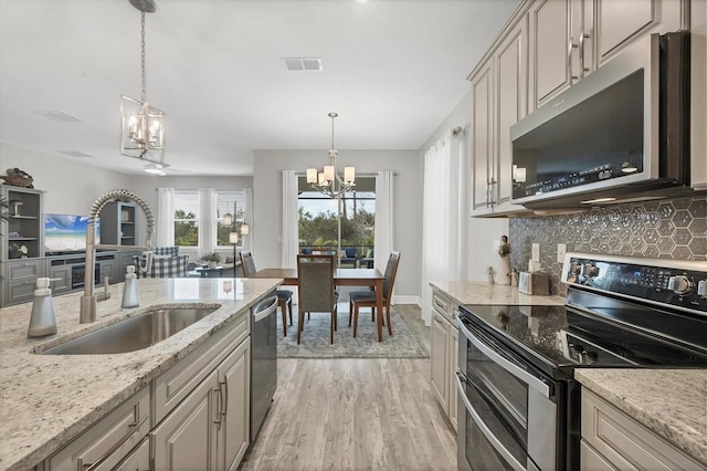 kitchen featuring appliances with stainless steel finishes, backsplash, hanging light fixtures, light hardwood / wood-style flooring, and sink