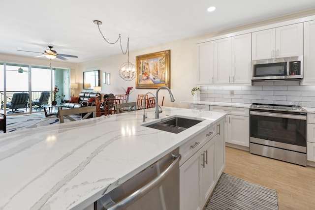 kitchen with sink, light stone counters, decorative light fixtures, ceiling fan with notable chandelier, and appliances with stainless steel finishes