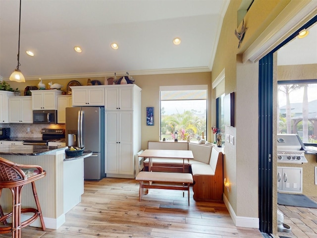 kitchen featuring a breakfast bar, hanging light fixtures, ornamental molding, stainless steel appliances, and white cabinets