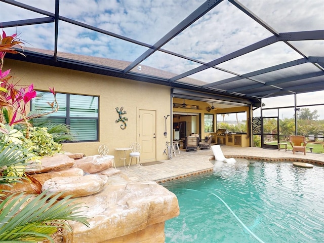 view of pool with exterior kitchen, a patio area, and glass enclosure