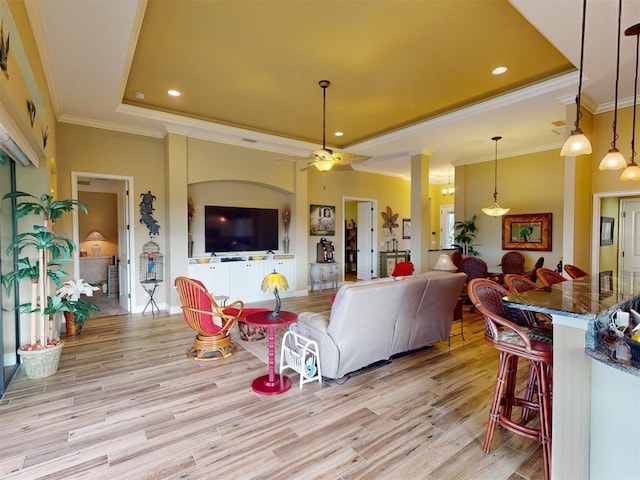 living room with a tray ceiling, light hardwood / wood-style flooring, ornamental molding, and ceiling fan