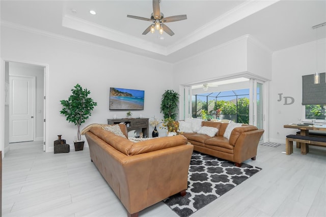 living room with a high ceiling, crown molding, light hardwood / wood-style flooring, ceiling fan, and a tray ceiling