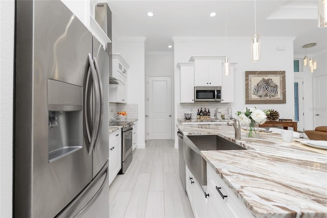 kitchen featuring decorative backsplash, ornamental molding, stainless steel appliances, decorative light fixtures, and white cabinetry