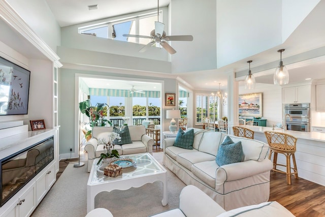 living room with ceiling fan with notable chandelier, dark hardwood / wood-style flooring, and high vaulted ceiling