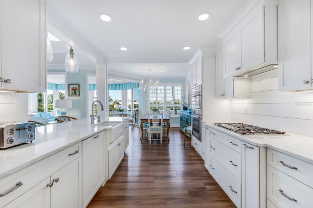 kitchen with pendant lighting, white cabinets, sink, light stone countertops, and stainless steel appliances