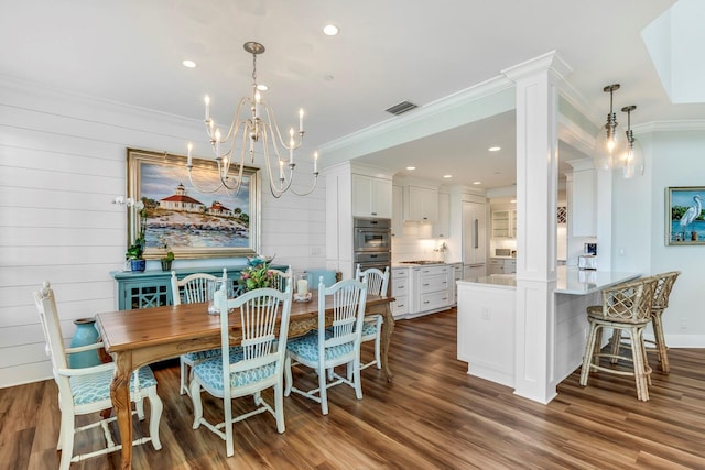 dining room with crown molding, ornate columns, dark wood-type flooring, and an inviting chandelier