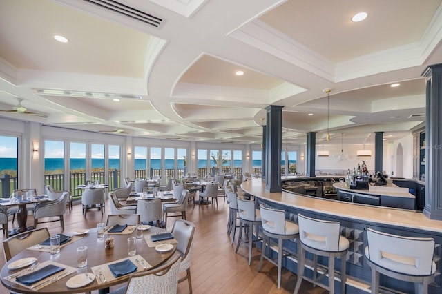 dining space with a healthy amount of sunlight, a water view, wood-type flooring, and coffered ceiling