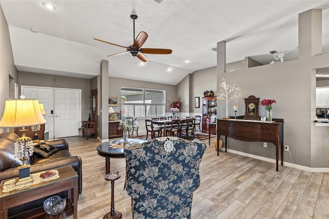 living room with ceiling fan, lofted ceiling, a textured ceiling, and light hardwood / wood-style flooring