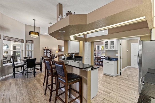 kitchen featuring hanging light fixtures, stainless steel fridge, light wood-type flooring, a notable chandelier, and white cabinetry