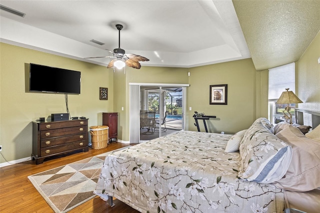 bedroom featuring access to exterior, ceiling fan, a textured ceiling, a tray ceiling, and hardwood / wood-style flooring