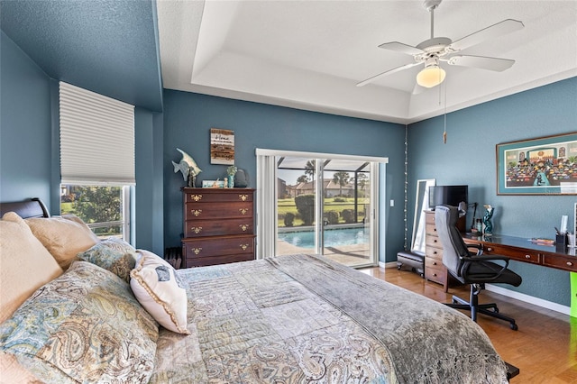 bedroom featuring a tray ceiling, multiple windows, ceiling fan, and access to outside