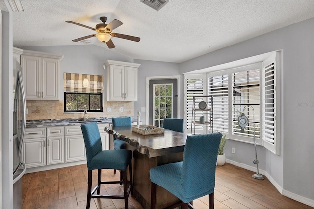 dining space with a textured ceiling, ceiling fan, sink, and lofted ceiling