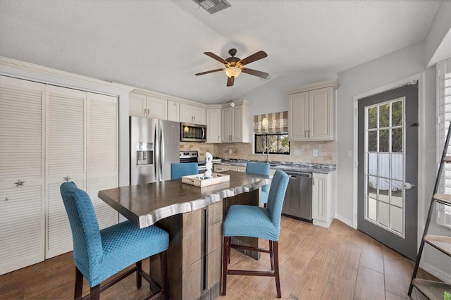 kitchen featuring lofted ceiling, light hardwood / wood-style flooring, ceiling fan, tasteful backsplash, and stainless steel appliances