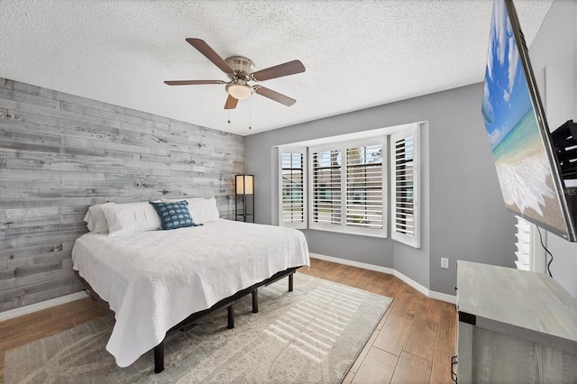 bedroom with wood walls, hardwood / wood-style floors, ceiling fan, and a textured ceiling