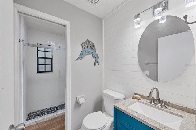 bathroom featuring vanity, wood walls, toilet, a textured ceiling, and tiled shower