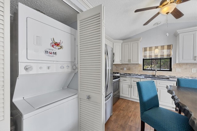 kitchen with lofted ceiling, stacked washer and clothes dryer, sink, stainless steel electric range oven, and white cabinetry