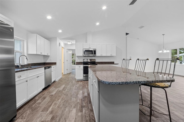 kitchen featuring appliances with stainless steel finishes, a center island, sink, white cabinetry, and lofted ceiling