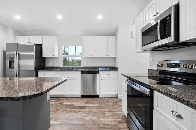 kitchen featuring stainless steel appliances, white cabinetry, and dark stone countertops