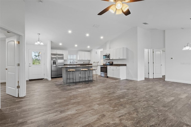 kitchen with a breakfast bar, a kitchen island, high vaulted ceiling, white cabinetry, and appliances with stainless steel finishes