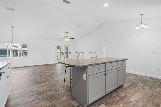 kitchen with gray cabinetry, ceiling fan with notable chandelier, a kitchen island, and pendant lighting