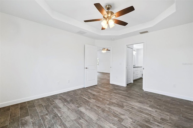 unfurnished bedroom with a raised ceiling, connected bathroom, and ceiling fan