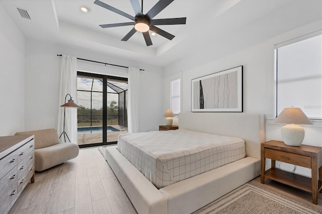 bedroom with ceiling fan, access to exterior, a raised ceiling, and light wood-type flooring