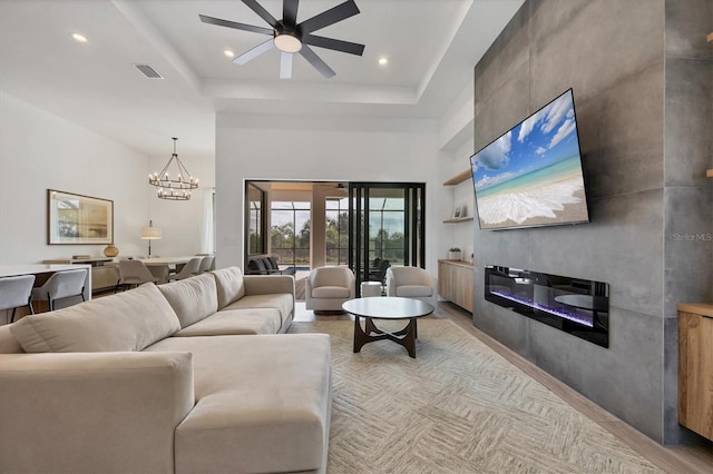 living room featuring a tray ceiling, a fireplace, ceiling fan with notable chandelier, and light hardwood / wood-style floors