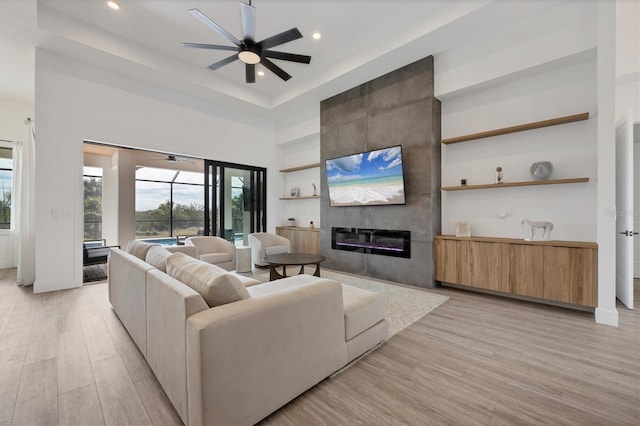 living room featuring ceiling fan, a high ceiling, a large fireplace, and light wood-type flooring