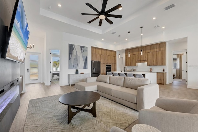 living room featuring a raised ceiling, ceiling fan with notable chandelier, a high ceiling, and light hardwood / wood-style floors