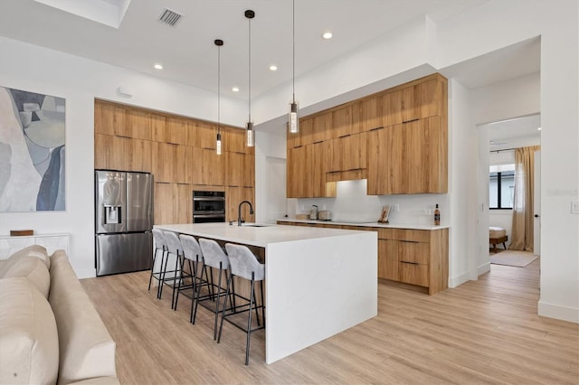 kitchen with a kitchen bar, stainless steel refrigerator with ice dispenser, a spacious island, pendant lighting, and sink