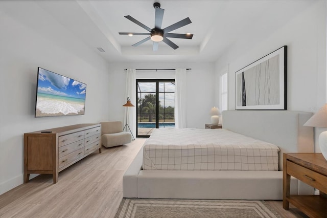 bedroom with light wood-type flooring, ceiling fan, a raised ceiling, and access to outside