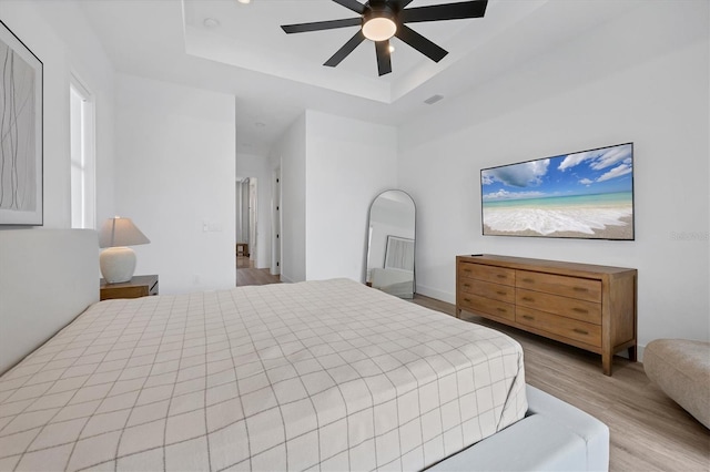 bedroom with ceiling fan, light hardwood / wood-style floors, and a tray ceiling