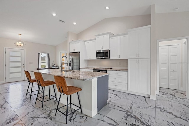 kitchen featuring a center island with sink, a breakfast bar, white cabinetry, light stone countertops, and appliances with stainless steel finishes