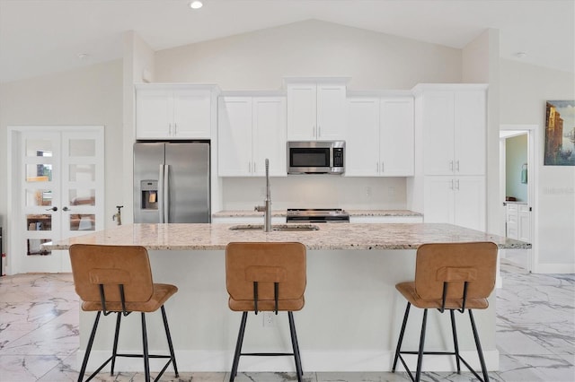 kitchen featuring white cabinets, appliances with stainless steel finishes, an island with sink, and light stone counters