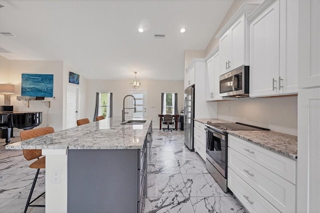 kitchen with a large island with sink, white cabinets, stainless steel appliances, sink, and a breakfast bar area