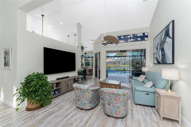 living room with ceiling fan, a towering ceiling, and light wood-type flooring