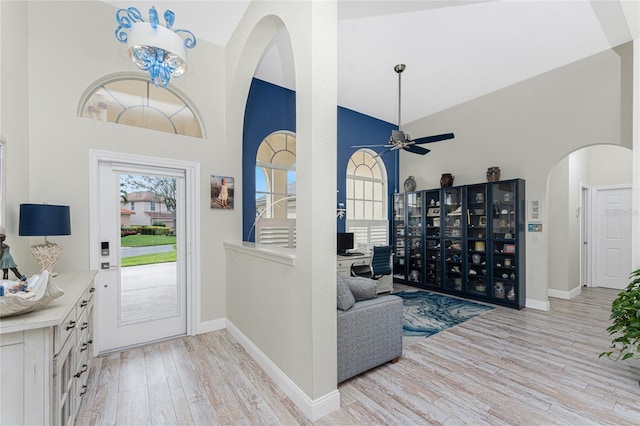 foyer featuring ceiling fan with notable chandelier, light hardwood / wood-style floors, and high vaulted ceiling